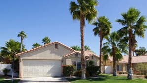 A single-story house with a garage, surrounded by palm trees and a well-maintained lawn.