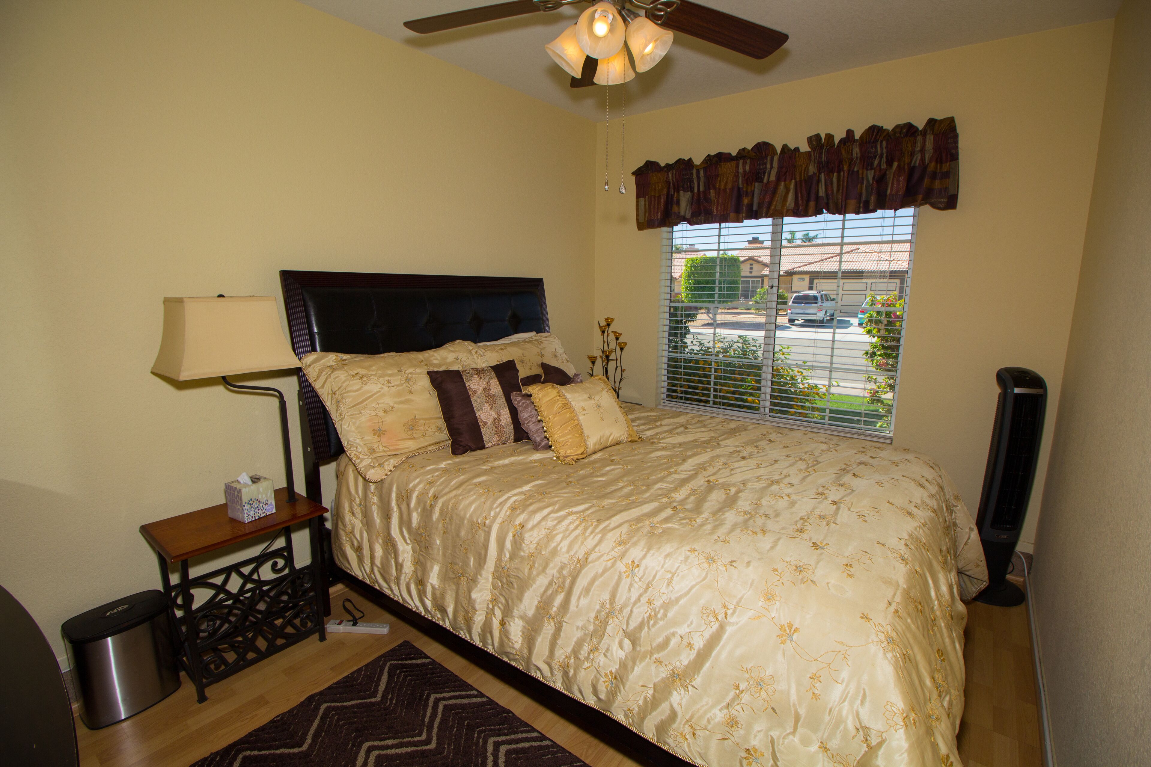 A bedroom with a bed, a nightstand, a lamp, a heater, and a window with a view of the outside.