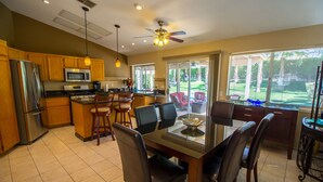 A kitchen with wooden cabinets, a stainless steel refrigerator, a microwave, and a dining area with a glass-top table and chairs.