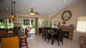A spacious kitchen with a dining area, a fireplace, and a large window overlooking a garden.