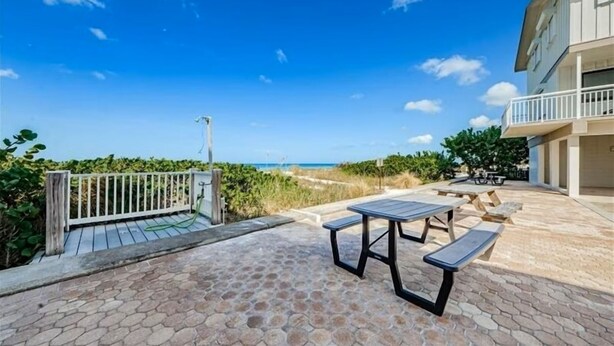 Un patio con una mesa y bancos con vista a la playa.