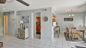 Un amplio espacio de sala con una mesa y sillas de comedor, una cocina al fondo y un ventilador de techo.