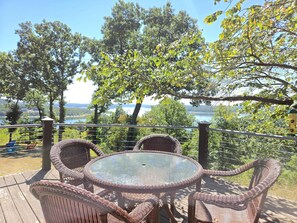 An outdoor deck with wicker furniture and a glass table, overlooking a lake and trees.