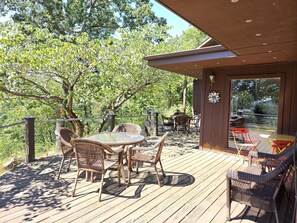 A wooden deck with wicker furniture and a glass table, overlooking a natural landscape.