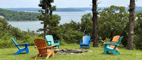 A lakeside view with four Adirondack chairs and a fire pit.