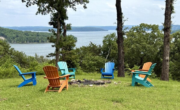 A lakeside view with four Adirondack chairs and a fire pit.