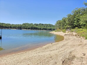 A natural landscape with a clear lake, a pebbly shore, and dense greenery in the background. - Lands End-Easy Private, lake access, with amazing lakeview. (Garfield)