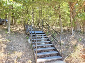 Un escalier en métal situé dans une zone boisée, avec des arbres et un véhicule en arrière-plan.