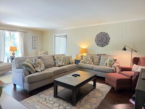 A living room with a sofa set, a coffee table, and a red armchair. There are two lamps on side tables, and a decorative wall piece is visible.