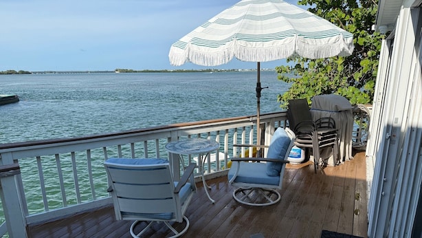 A deck with a view of the water, a table, two chairs, and an umbrella. - Springs Venture Out Dolphin House #386 with beautiful open water views (Cudjoe Key)