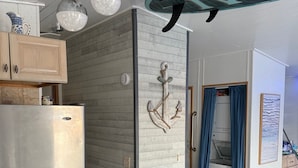 A modern kitchen with a stainless steel refrigerator, wooden cabinets, and a decorative anchor wall art piece. - Springs Venture Out Dolphin House #386 with beautiful open water views (Cudjoe Key)