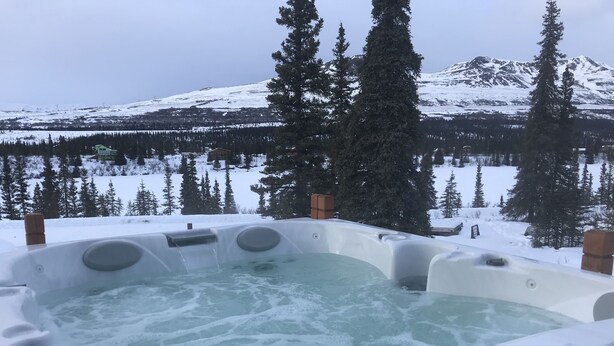 A hot tub with a view of a snowy mountain and forest.