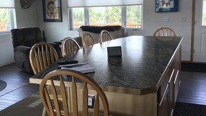 A modern kitchen with a large island, wooden chairs, and a deer head mounted on the wall.