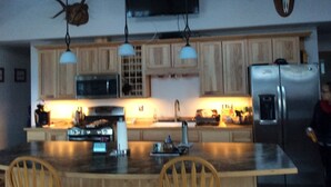 A kitchen with wooden cabinets, a stainless steel refrigerator, a microwave, and a flat-screen TV mounted on the wall.