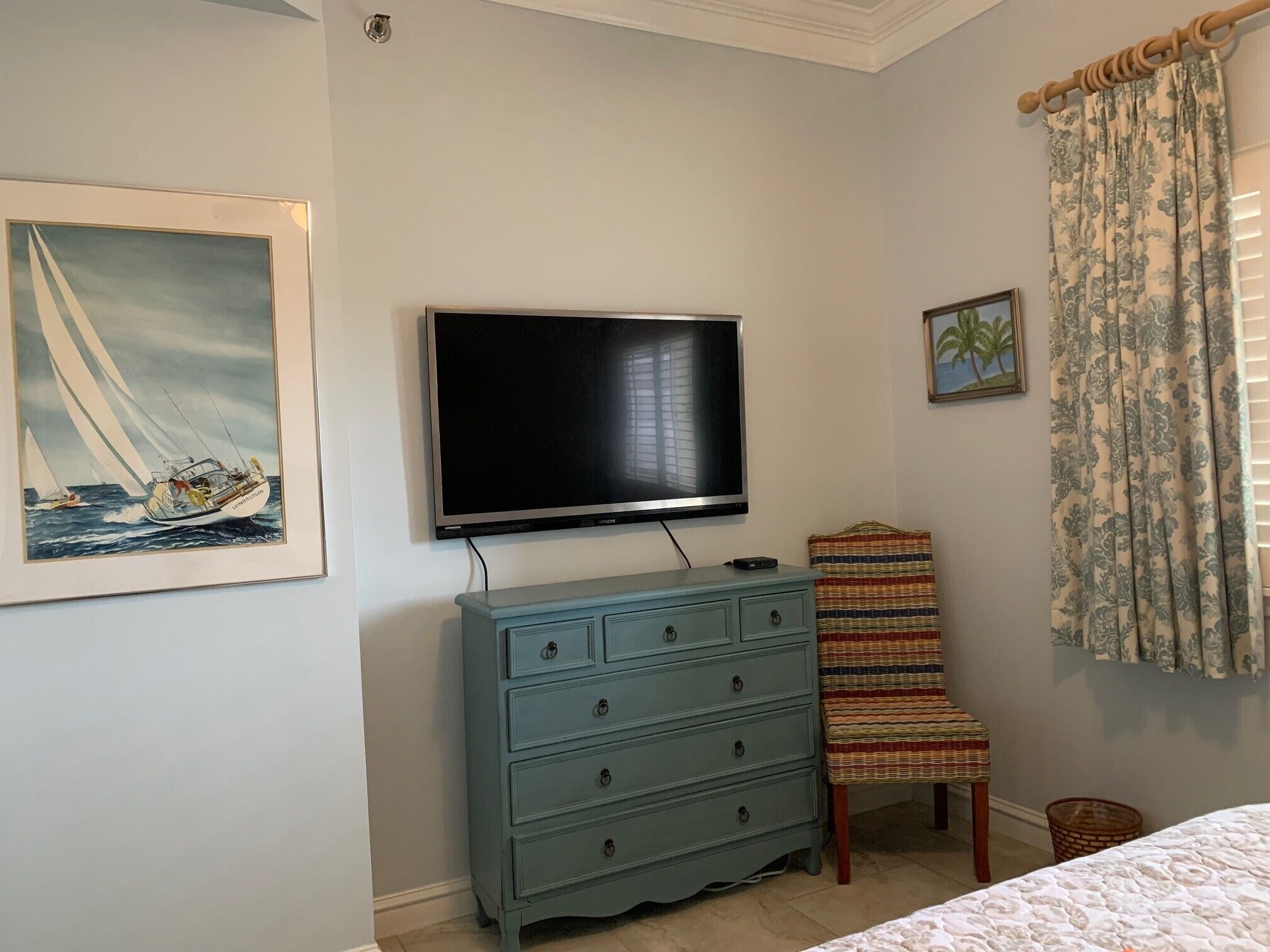 Un dormitorio con una televisión montada en la pared, un aparador, una silla y una cama.