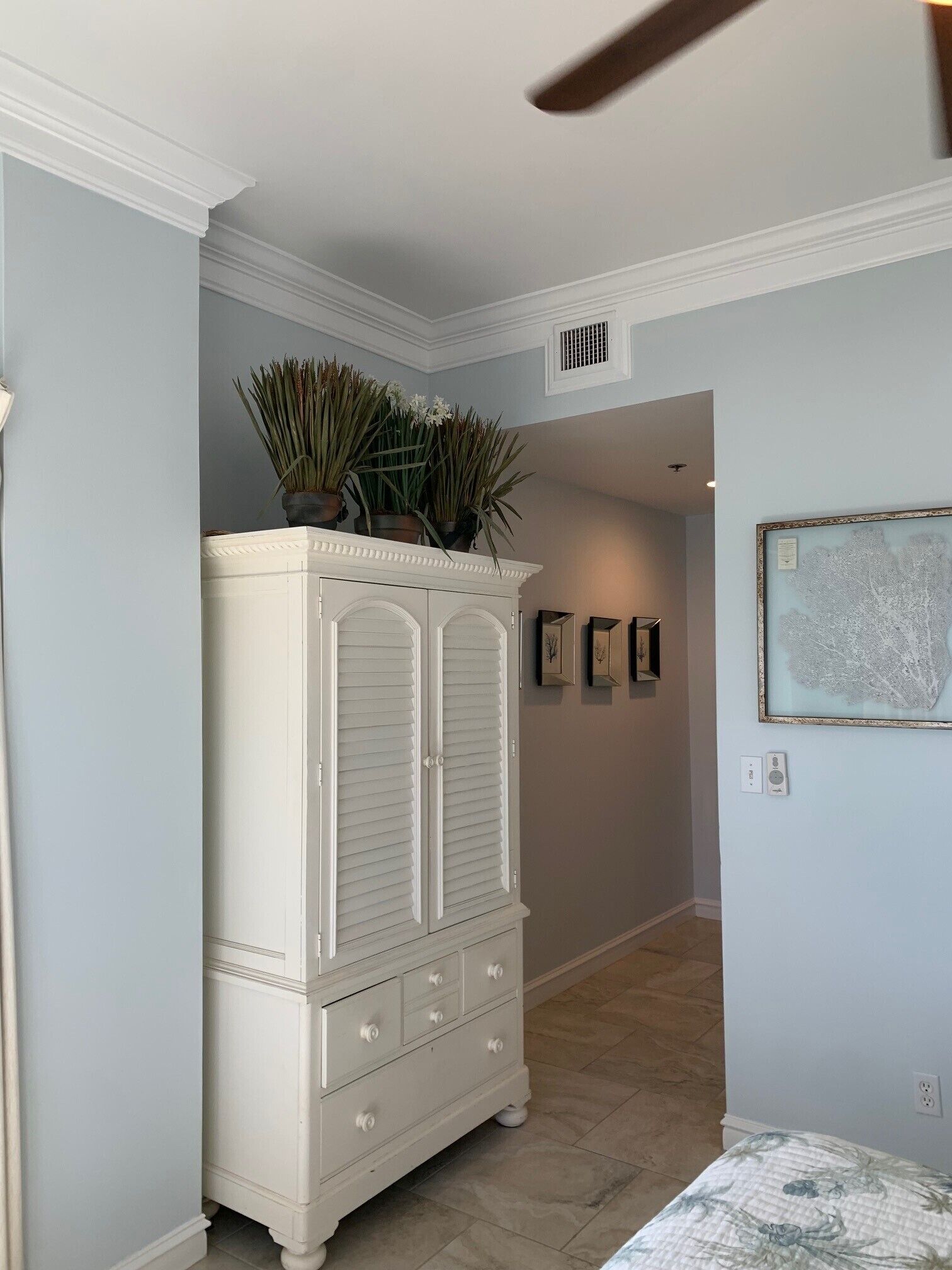 A hallway with a white armoire, a ceiling fan, and a framed artwork on the wall.
