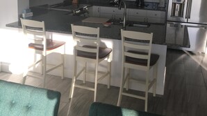A modern kitchen with white cabinets, a central island with seating, a microwave, and a refrigerator.