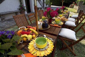 Una mesa de madera al aire libre con varias frutas, un tazón y una jarrón.