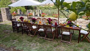 An outdoor dining area with stone walls, wooden chairs, and tables set with flowers, fruits, and beverages. - Historic panoramic villa near Lucca (Lucca)