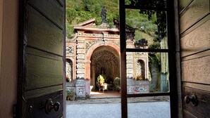 An open door revealing a courtyard with a statue, a stone archway, and potted plants. - Historic panoramic villa near Lucca (Lucca)