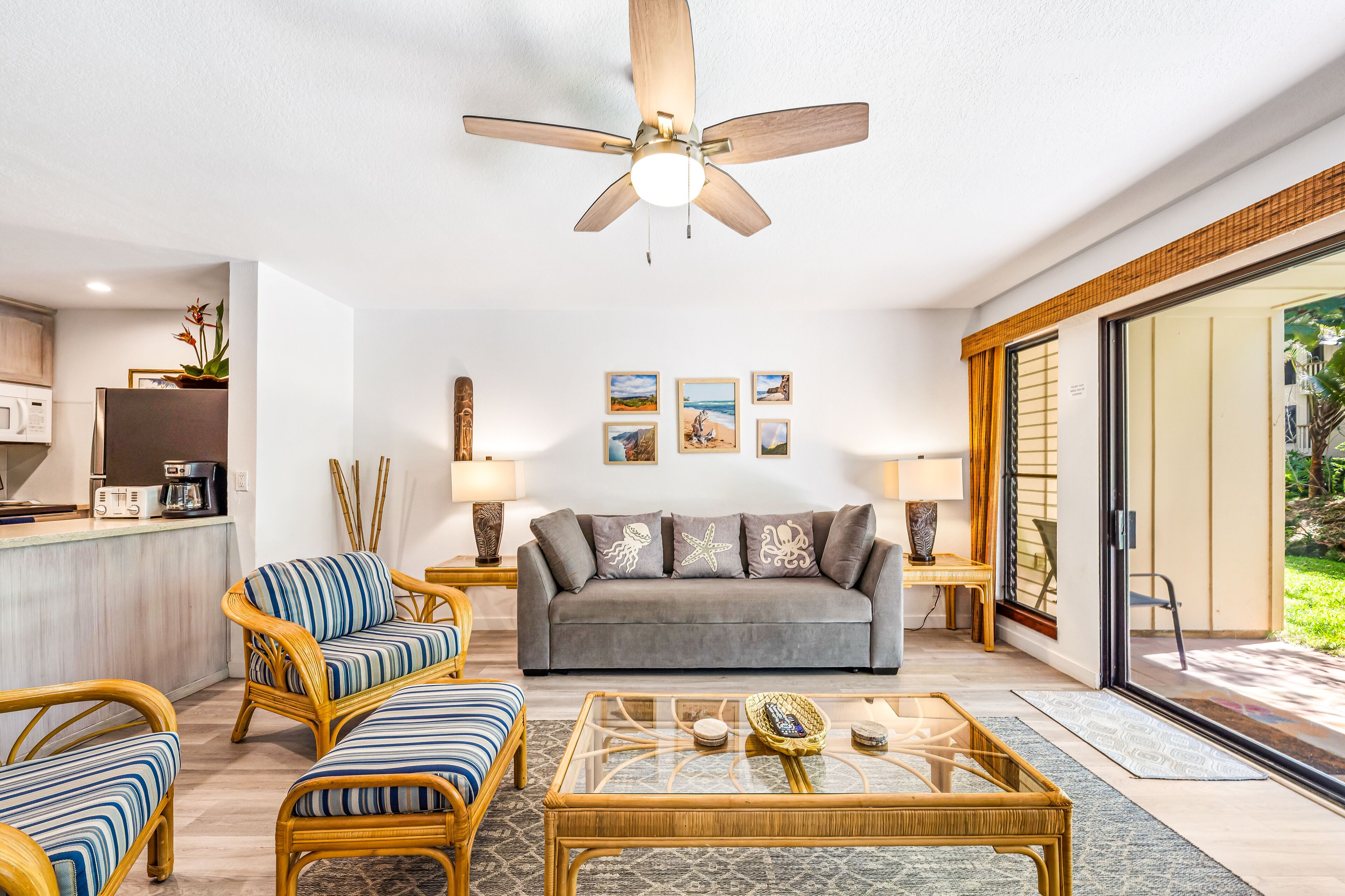 A modern living room with a grey sofa, striped armchairs, a glass coffee table, and a ceiling fan.