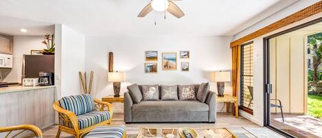 A modern living room with a grey sofa, striped armchairs, a glass coffee table, and a ceiling fan.