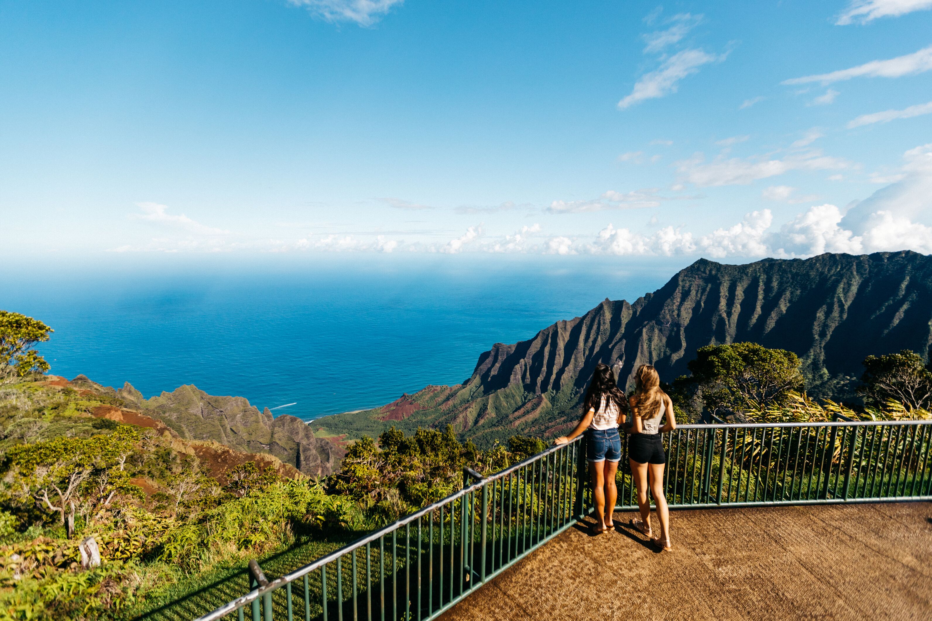 Un mirador panorámico con barandilla metálica, que domina una costa montañosa y el océano.