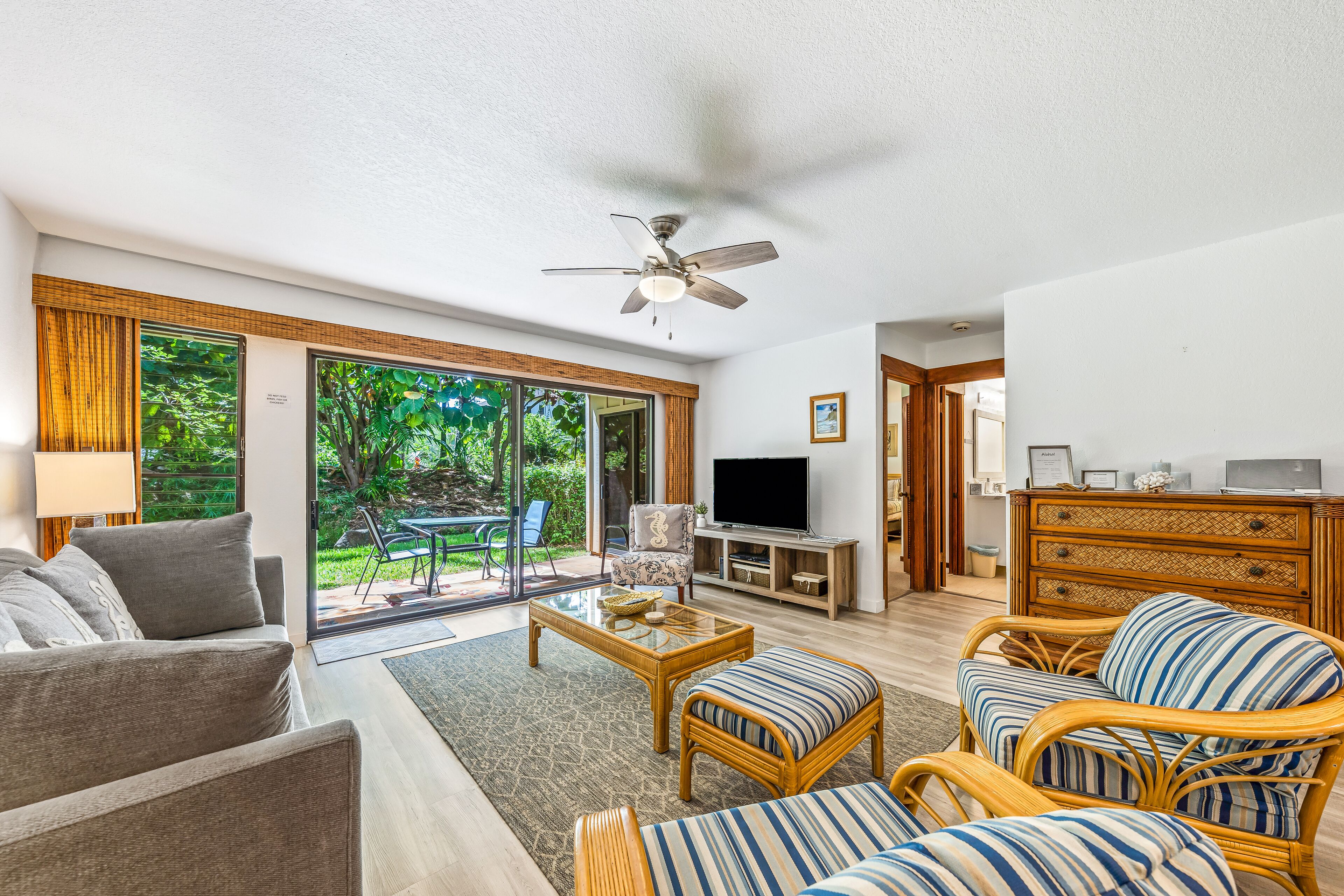 A spacious living room with a sofa, two striped armchairs, a coffee table, a television, and a ceiling fan.