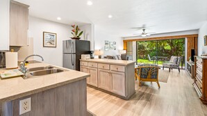 A modern kitchen with a central island, a dining area with a chair, and a view of greenery through large windows.