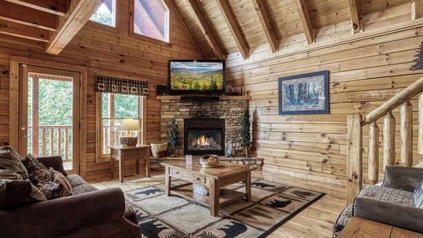 Interior acogedor de una cabaña con chimenea de piedra, paredes de madera, un televisor montado encima y una zona de estar confortable con un sofá y una mesa de centro.