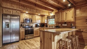 Una cocina de estilo cabaña de madera con una isla central, taburetes de bar, electrodomésticos de acero inoxidable y armarios de madera.