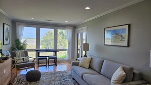Uma sala de estar espaçosa com uma janela grande, um sofá cinza, uma mesa de jantar e vista para o exterior.
