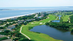 Um campo de golfe com um corpo de água, rodeado por áreas residenciais e uma praia.