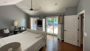 Un dormitorio con cama, ventilador de techo, televisión y puerta corrediza de vidrio que da a un área exterior.