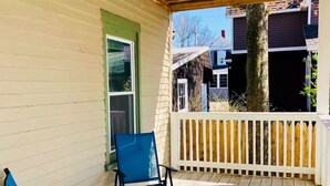 A covered porch with two blue chairs and a small table, wooden railing, and a view of neighboring houses. - Delightful Beachside two-bedroom apartment (Old Orchard Beach)