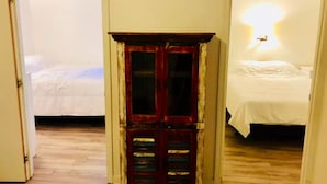A hallway with a wooden cabinet, a bed with white bedding, and a wall-mounted light fixture. - Delightful Beachside two-bedroom apartment (Old Orchard Beach)