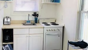 A compact kitchen with white cabinets, a stove, a toaster, and a window with blinds. - Delightful Beachside two-bedroom apartment (Old Orchard Beach)