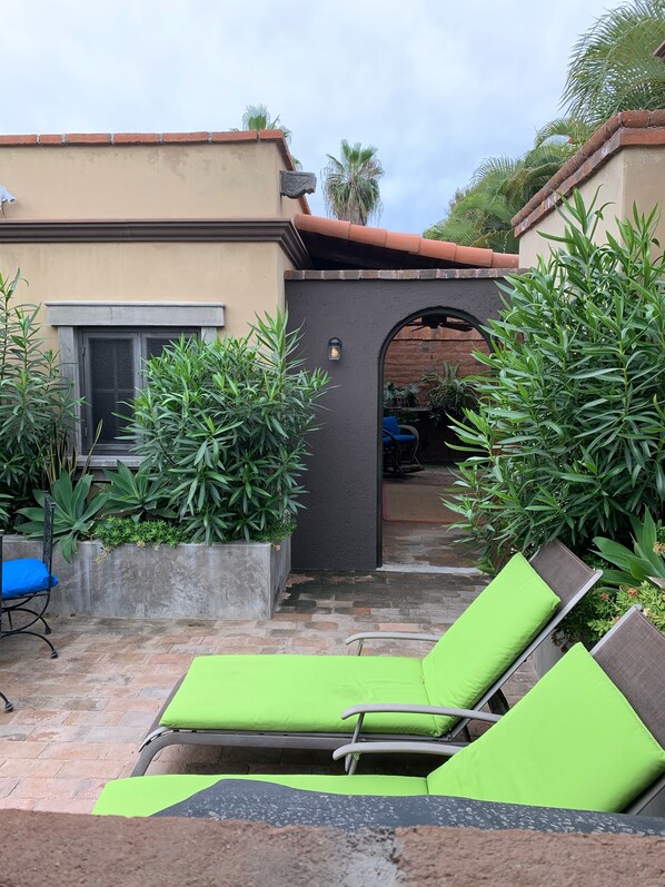 A patio area with two green lounge chairs, a concrete planter with plants, and a brick wall.