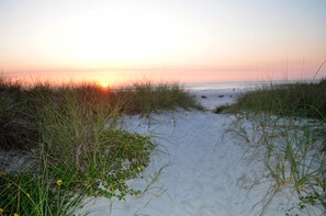A beach path with sand and grass leading to the ocean.