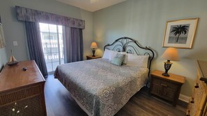 Une chambre d’hôtel avec un grand lit, deux tables de chevet avec des lampes, une commode en bois, une fenêtre avec des rideaux et un tableau encadré au mur.