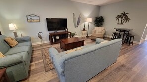 Sala de estar com sofá, mesa de centro, televisão, luminária, poltrona e mesa com banquetas.
