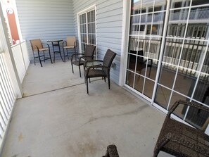 A covered patio area with wicker furniture, a glass door, and a view of a building with balconies.