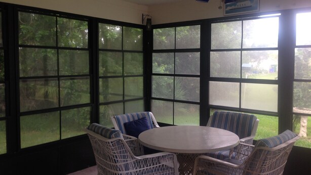 A sunroom with a large window, wicker furniture, and a ceiling fan. - Comfy House Near River And Beach (Sebastian)