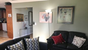 A living room with a black leather sofa, patterned cushions, a red pillow, and two framed artworks on the wall. - Comfy House Near River And Beach (Sebastian)