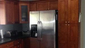 A kitchen with wooden cabinets, a stainless steel refrigerator, and a black countertop. - Comfy House Near River And Beach (Sebastian)