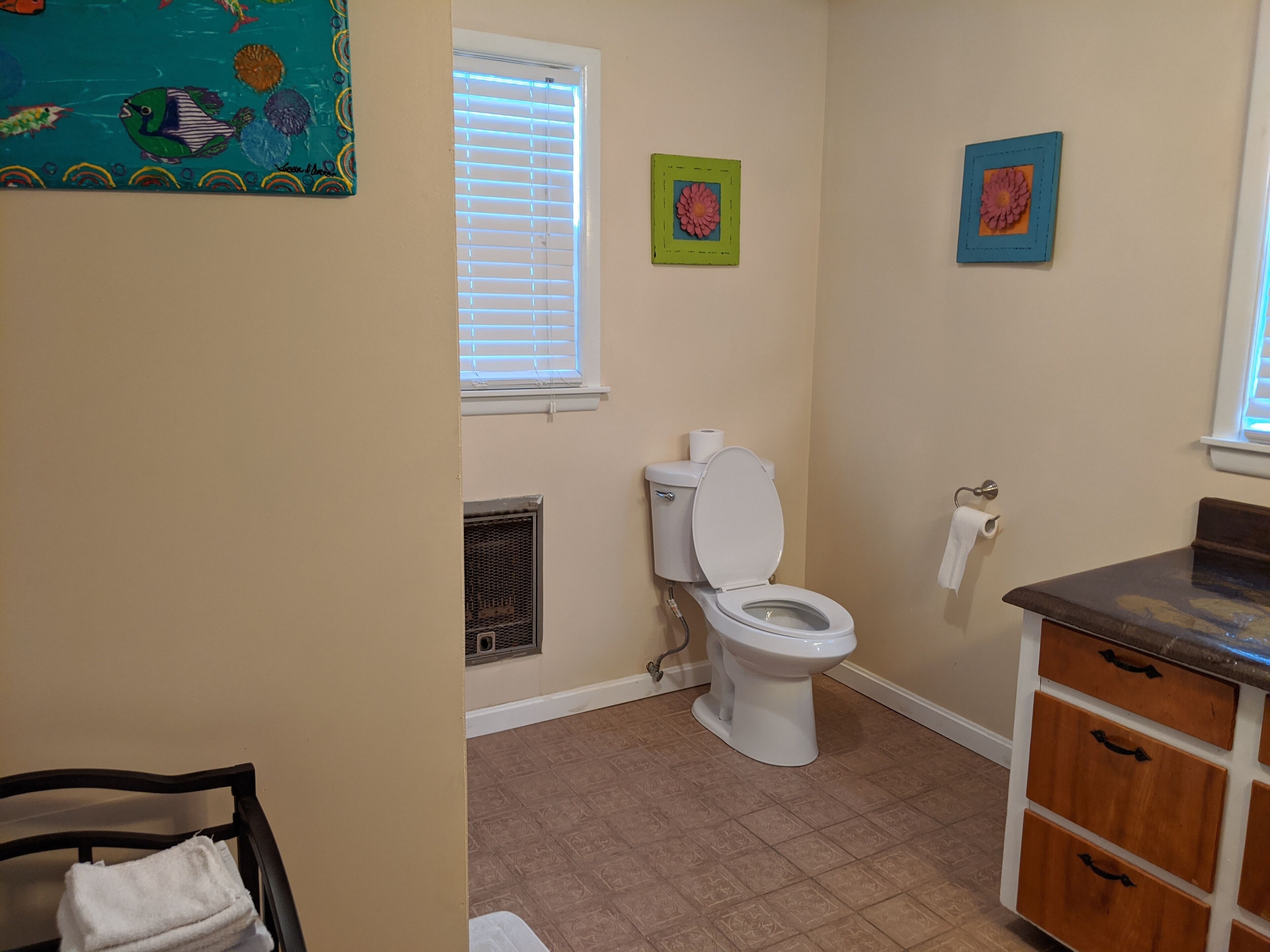 Un baño con inodoro, ventana con persianas, radiador y lavamanos con encimera.