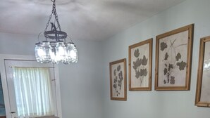 A dining room with a wooden table and four chairs, a chandelier, and three framed botanical prints on the wall.
