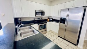 Una cocina moderna con armarios blancos, electrodomésticos de acero inoxidable, encimera negra y suelo de baldosas.