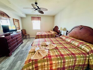 Une chambre d’hôtel avec deux lits, une commode, un téléviseur et un ventilateur de plafond.