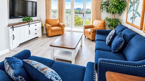 Una sala de estar con un televisor de pantalla plana, sillones de cuero, un sofá azul y un amplio ventanal con cortinas.